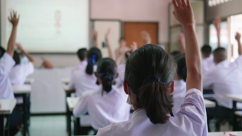 Slow motion of Asian high school students in white uniform actively study science by raising their hands to answer questions on projector screen that teachers ask them  in science classroom.
