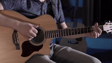 man with a beard plays acoustic guitar in a music studio. Closeup of guitar strings and neck