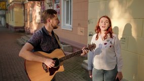 duet of young musicians. A man with a beard plays the acoustic guitar, a red haired woman sings. Town. Summer evening. Sunset - Powered by Shutterstock - Get 15% off with code: PIKWIZARD15