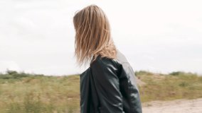 Happy beautiful woman running on camera in dress and Leather Jacket, woman brown hair blowing in wind.  Feeling of freedom and independence. 