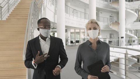 Business people wearing face mask meeting in modern corporate office lobby and walking