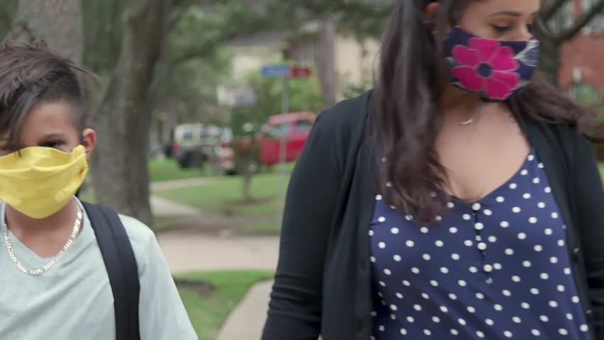 Prerequisite for in classroom instruction and the new normal during COVID19 pandemic is mask wearing as demonstrated by this mother and her children as she walks them to the school bus stop.