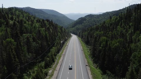 Soaring over long stretch of highway in the middle of a lush green forest with rolling hills and mountains as far as the eye can see