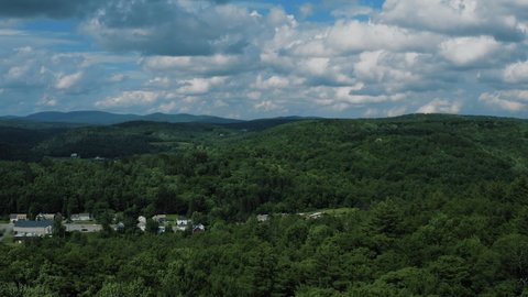 Aerial shot of a beautiful small town in Vermont with lush green trees, large blue mountains and strong winds