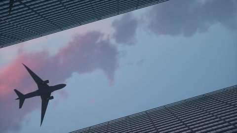 Low angle rotating camera with a airplane flying over the top big city skyscraper office buildings