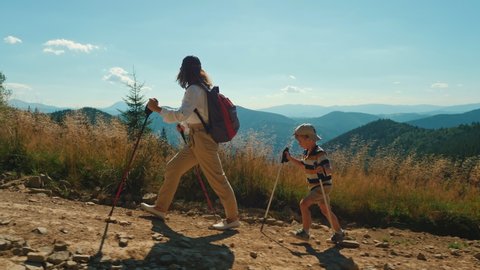 Active mother with her little son climbing mountain. Woman and child with trekking poles and backpack hike together along a rocky path