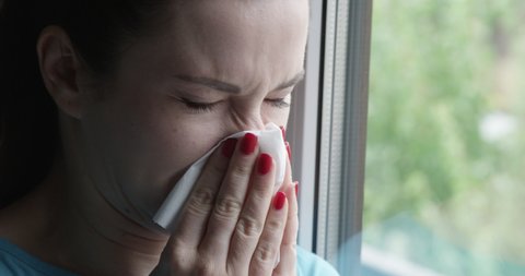 Woman Sneezing into a Napkin Standing by the Window