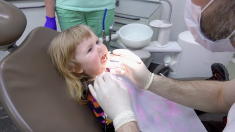 The dentist asks a little girl to open the mouth and show her teeth. The Dental Clinic