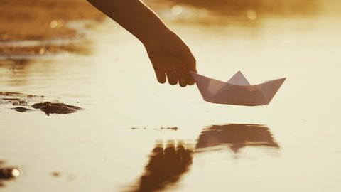child puts a paper boat into the water. happy family fantasy kid dream concept. child playing with paper boat ship. a child hand launches a boat in a park in a lifestyle pond