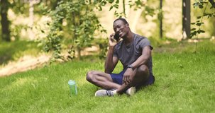 Cheerful african american guy talking on cellphone, resting on grass in park