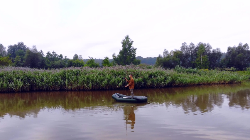 young man fishing in the middle lake standing on a boat. fisherman holds a rod or spinning in hands. the river in the water. Recreation and hobbies in nature. Active rest. spins bended rod