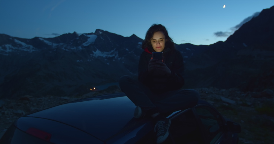 Woman communicates online, typing text on the phone, millennial sitting in a car in the mountains in nature, manager enjoys a vacation in Europe, travel and remote work concept