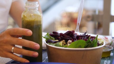 Hand taking a bottle of green smoothie. Healthy vegan lunch at the food court: green smoothie and a salad. Healthy ready to eat food