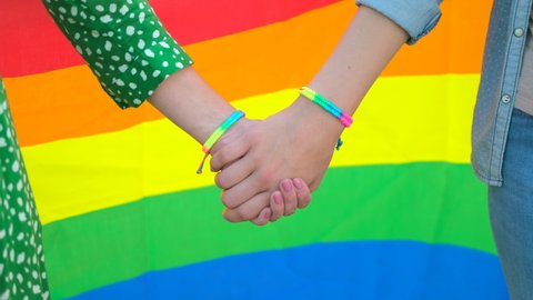 Two lesbian woman holding hands isolated on background rainbow LGBT lgbt flag gay pride flag - gay, bisexual, transgender movements. Concept of happiness, freedom, love same-sex couple, 4 K slow-mo