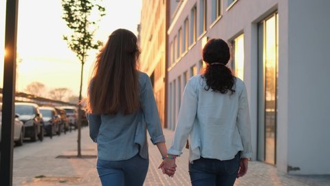 Two lesbian woman couple holding hands on street outdoors. Rainbow LGBT lgbt flag gay pride - gay lesbians bisexual transgender movements. Concept happiness, freedom, love same-sex couple, 4 K slow-mo