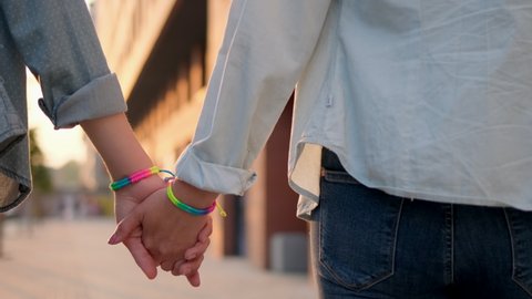Two lesbian woman couple holding hands on street outdoors. Close-up Rainbow LGBT lgbt flag gay pride - gay, bisexual, transgender. Concept happiness, freedom, love same-sex couple, 4 K slow-mo