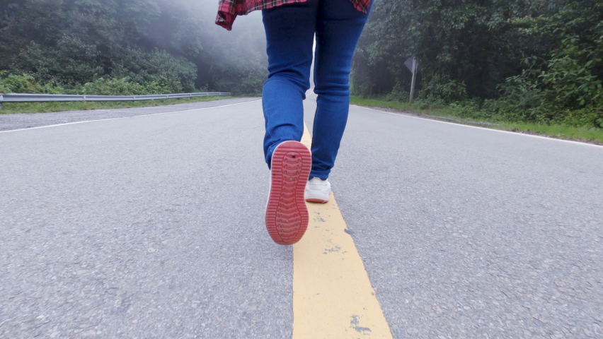 Close-up rear of female traveler feet walking on asphalt road among nature around. Royalty-Free Stock Footage #1058395699