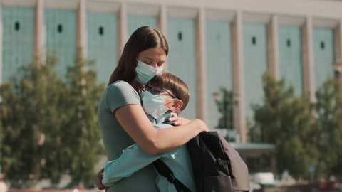  Back to school, Happy schoolboy, Learn lessons. A woman in a mask takes her child to school and hugs him. School season during a pandemic