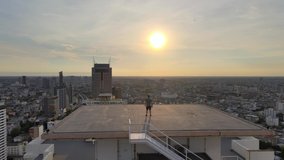 Man standing on top of a building rooftop, overlooking the city skyline at sunset, drone fly over - Powered by Shutterstock - Get 15% off with code: PIKWIZARD15