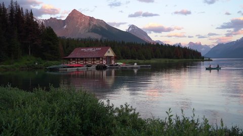 Jasper National Park, Canada - August 12, 2020: Panoramic view of Maligne Lake showing historic boathouse and tourists canoeing on the lake at sunset in Jasper National Park, Alberta, Canada.
