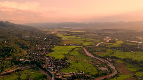 Aerial crane shot of village hills and rice fields on both sides of the river during evening sunset at Mae Sariang district Mae Hong Son province amazing Thailand.