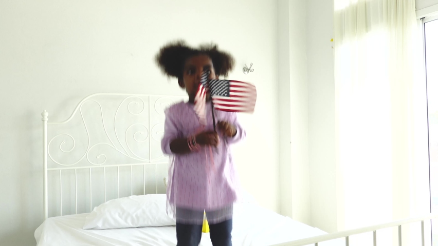 Happy cute active little african american kid girl holding american flag on bed Royalty-Free Stock Footage #1058399335
