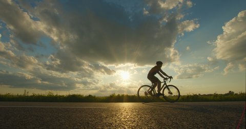 A cyclist is riding a bicycle on the highway. Sunset in the background. The camera moves back. 4K