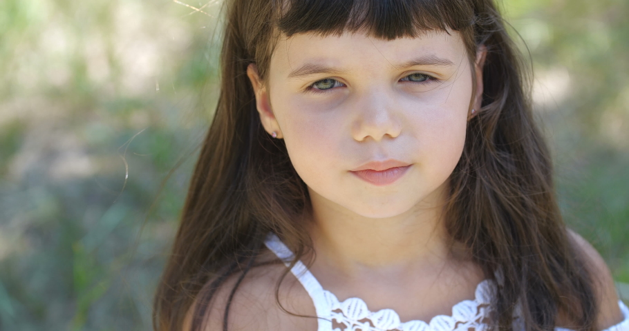 Close-up portrait of a blue-eyed girl dressed in white dress. She is praying with her hands clasped on sunny summer day. Little child makes a cherished wish with closed eyes. Pray for peace in Ukraine Royalty-Free Stock Footage #1058406202