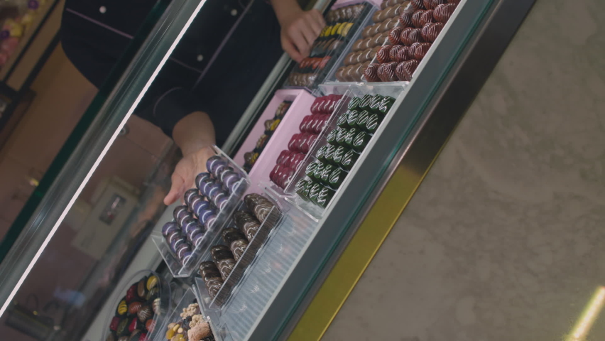 Huge counter with sweets chocolate: The employee puts the box full of chocolate in the chocolate fridge for the customers Royalty-Free Stock Footage #1058406910