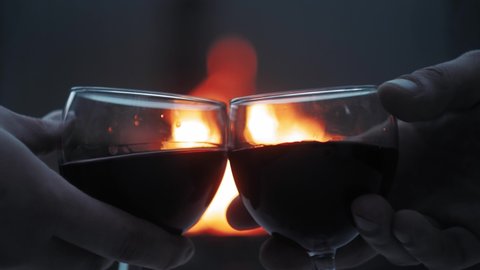 Two people raise glasses with wine and say cheers , say a toast, celebrate. Close up hands holding up glasses of red wine on bonfire background. Cheers concept.