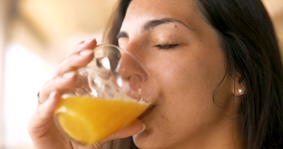 Authentic close up shot of an young brunette woman is drinking a fresh healthy dietetic biological natural orange juice from a transparent glass  taking a breakfast in the morning.