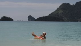 Slow motion: Young woman floating on inflatable ring wearing a red Santa Claus hat on vacation on a tropical island. 