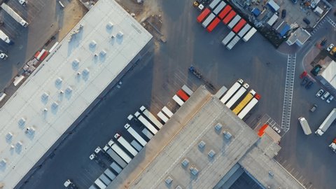 Aerial top down view of the big logistics park with warehouses, loading hub and a lot of semi trucks with cargo trailers awaiting for loading/unloading goods on ramps