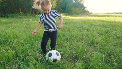 baby daughter playing football soccer in the park on the grass. happy family dream kid concept. little girl child play ball outdoor lifestyle sports in park healthy. kid play with son fun into ball