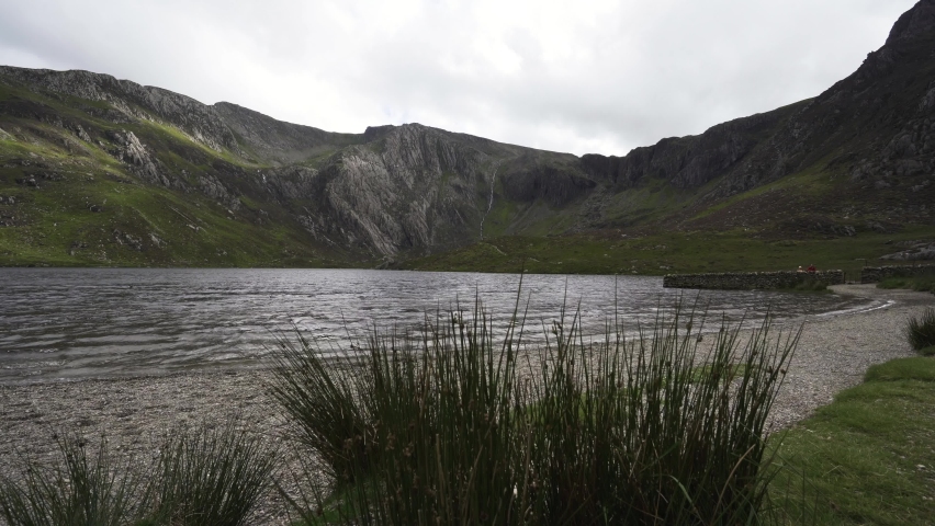Man walking in the Snowdonia mountains beside a lake with waves and beach