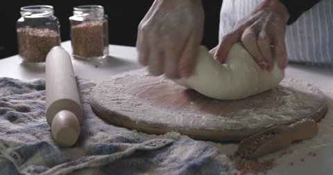 Close up view of baker kneading dough in flour on table. Hands of female chef kneading floured dough for bread.