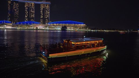 SINGAPORE - JANUARY 10, 2020: Touristic boat sailing in Marina Bay. People enjoying night cityscape with illuminated integrated resort Marina Bay Sands