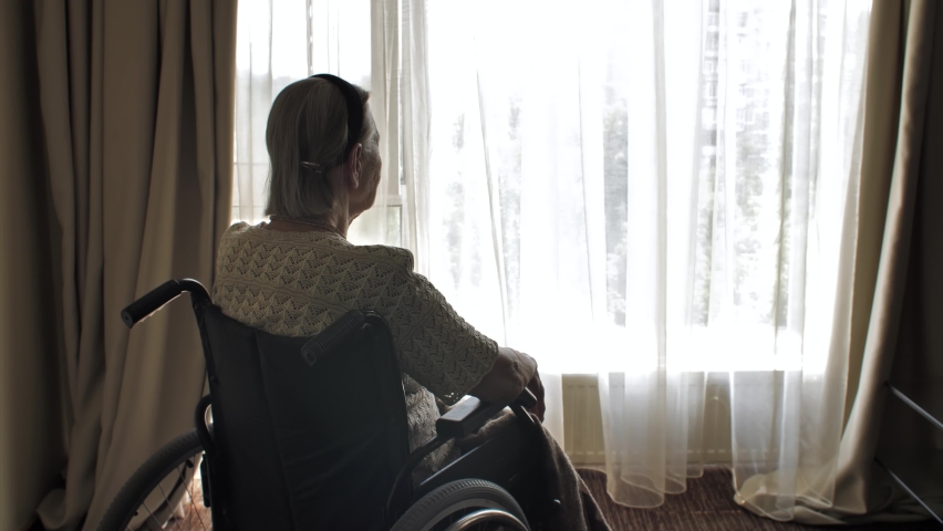 Disabled woman sit on wheelchair and looks through the window Royalty-Free Stock Footage #1058414500