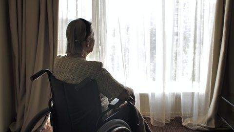 Disabled woman sit on wheelchair and looks through the window