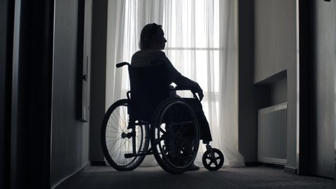 Old woman sit on wheelchair in a front of the window
