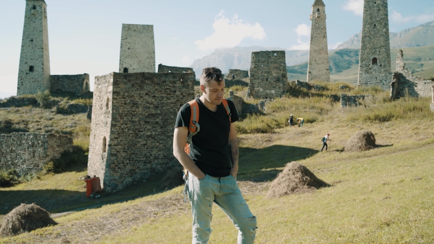 Traveler standing near ancient ruins in mountains. Young male tourist with backpack standing