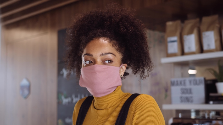 Medium eye shot of Female African coffee shop owner wearing face visor standing behind of counter and Sneeze Guard Royalty-Free Stock Footage #1058419363