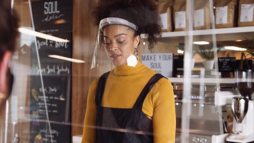 Eye Level Medium Close up, Female African coffee shop owner wearing face visor welcoming a customer. | Shutterstock HD Video #1058419381