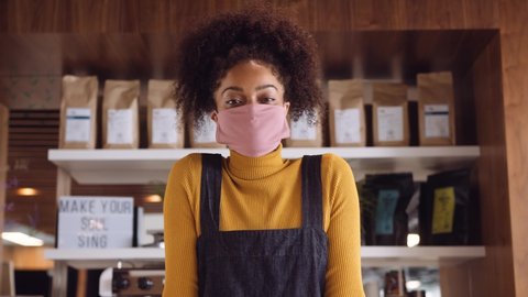 Female African coffee shop owner wearing face mask walking up and leaning on counter