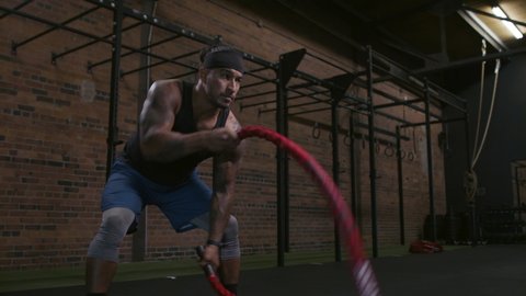 Focus on your goals! A diverse athlete uses power and speed to exercise. Ropes in a gym working arms. Maximum focus. Shot in 4k.  