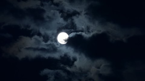  Full moon shining bright behind clouds at dark night. Time lapse