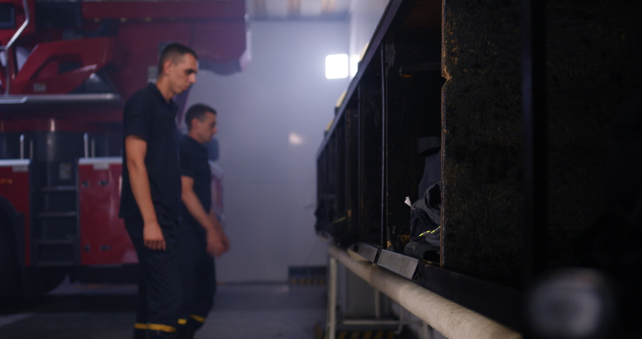 Zoom out view of group of firefighters standing near shelves and putting on uniform while preparing to ride on call in fire station Royalty-Free Stock Footage #1058424283