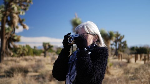 An older adult woman photographer taking pictures with her old fashioned film camera in a desert wildlife landscape.