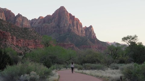 Woman walking away on trail towards the Watchman in Zion National Park, Utah in evening - slow motion