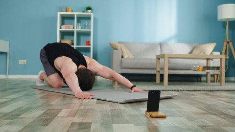 Young athletic man practices cobra pose at home, enjoying online yoga course for beginners, stretching his body, maintaining his physical shape, releasing stress, Slow motion.